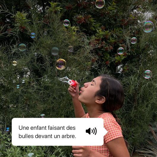 VoiceOver décrivant une photo et affichant la sortie vocale. ? Une enfant faisant des bulles devant un arbre. ?