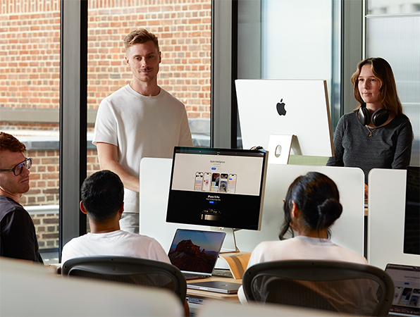 Five Apple colleagues gathered around their desks in conversation.