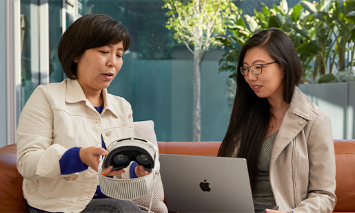 Jessica using a MacBook inside with a door open to the patio, sitting with an Apple colleague, who is showing her Apple Vision Pro.