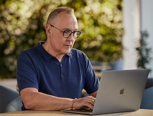 An Apple Software and Services employee working outside on a MacBook with greenery in the background.