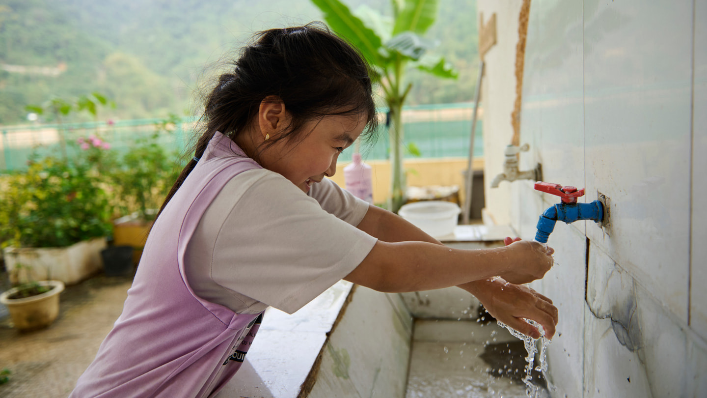 A student washes their hands outdoors in a large basin with a spigot at the Hi?n L??ng Primary and Secondary School.