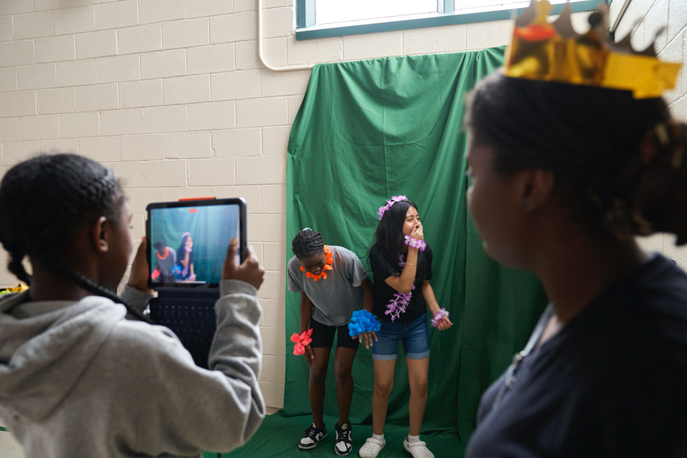 Estudiantes del campamento STEM Explorers posan frente a una pantalla verde mientras una participante les toma una foto con el iPad.