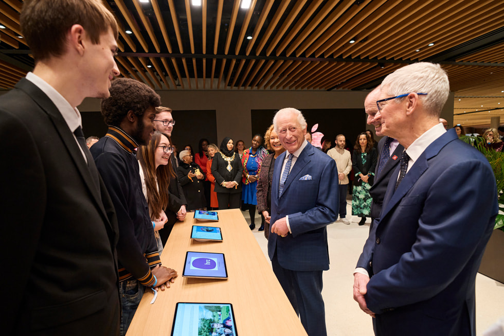 King Charles and Tim Cook meet alumni from The King’s Trust, who stand behind a table with iPad devices.